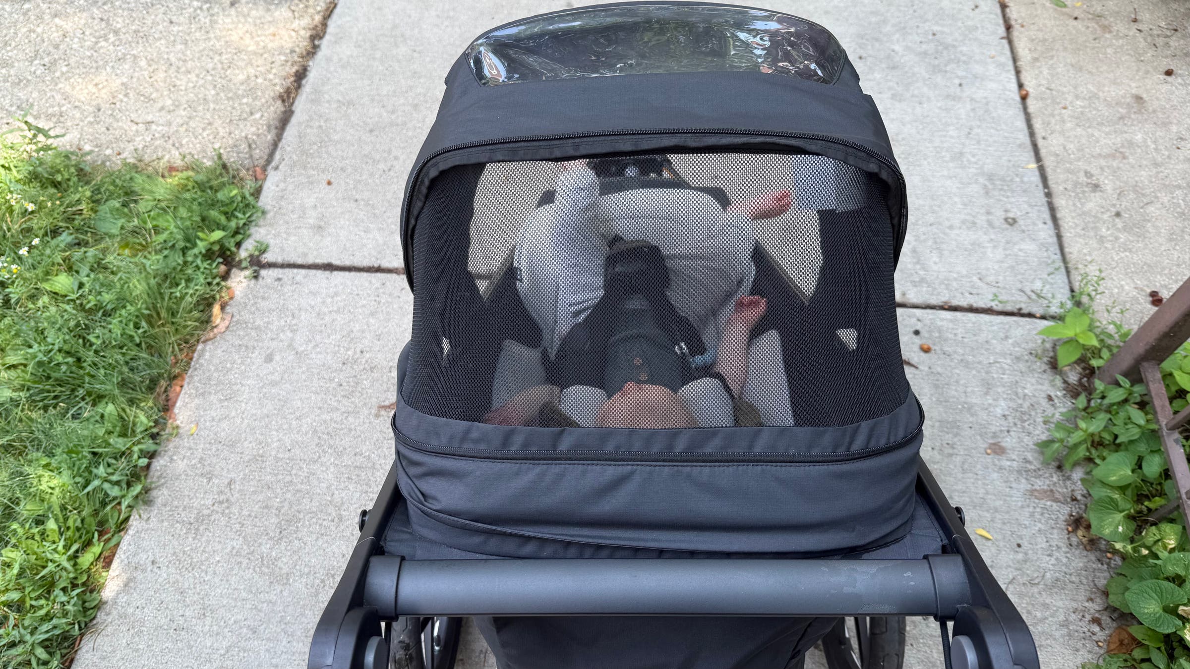 Top-down view of a baby riding in the Thule Urban Glide 3 jogging stroller, seen through the mesh canopy window while rolling along a sidewalk, highlighting the stroller’s ventilated sunshade and ergonomic handlebar design.