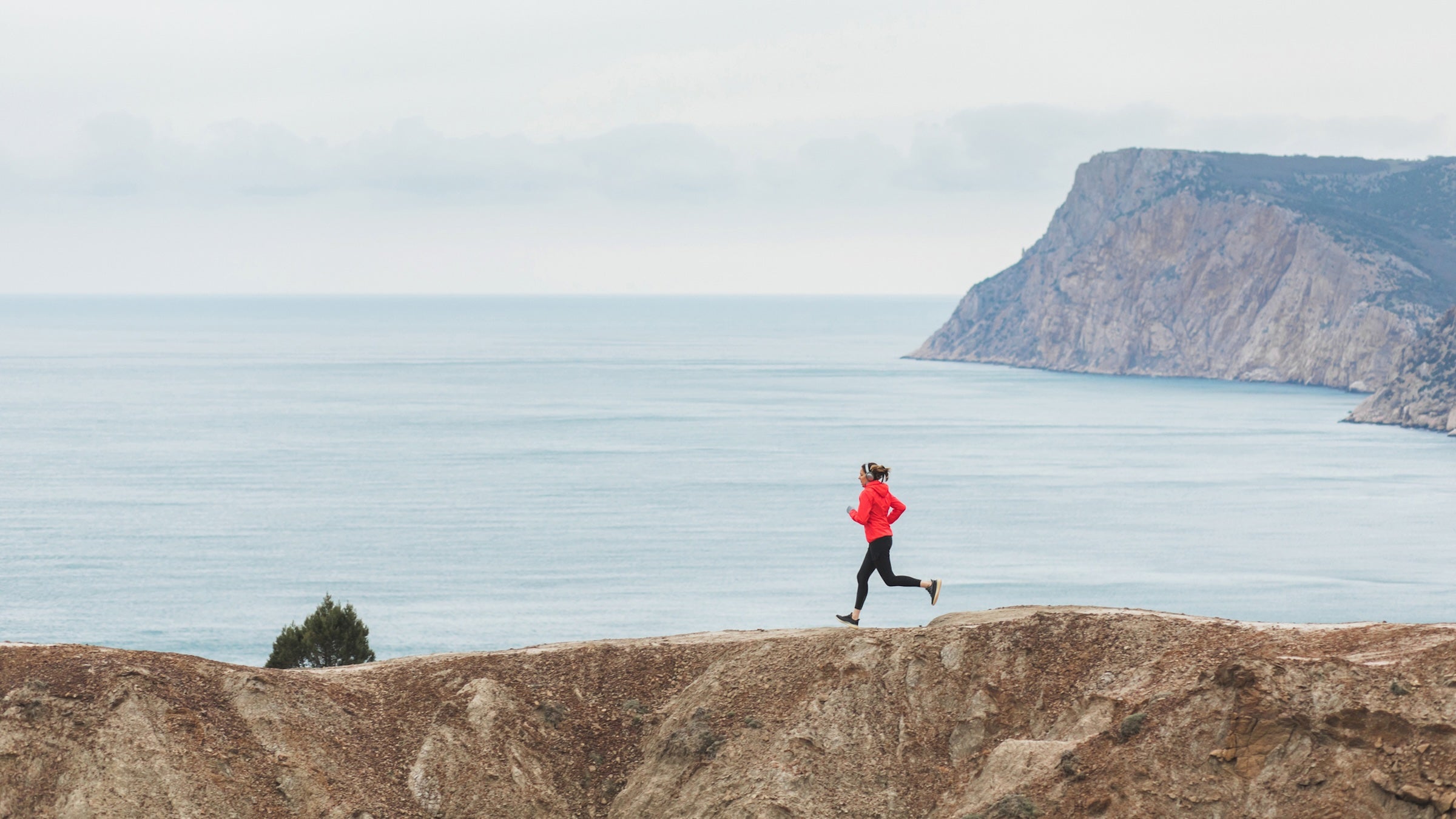 Woman trail running in mountains with scenery view of sea and coastline