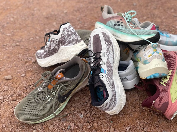 a pile of colorful road to trail and gravel running shoes on a dirt path