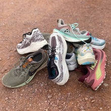 a pile of colorful road to trail and gravel running shoes on a dirt path