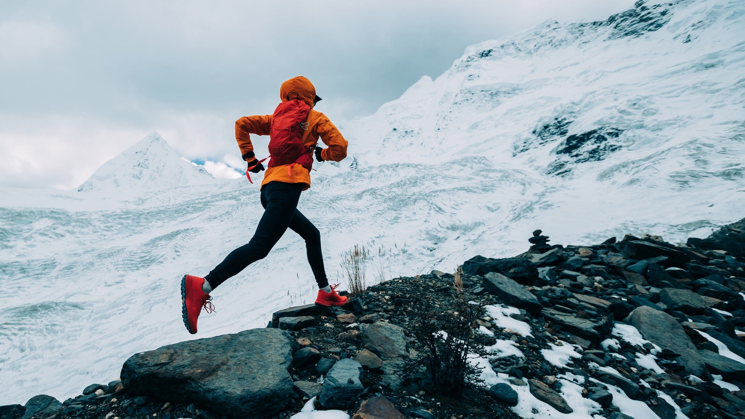 Woman trail runner cross country running up to winter snow mountain top