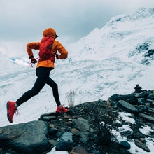 Woman trail runner cross country running up to winter snow mountain top