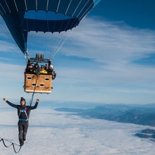 Friedi Kühne seen walking a slackline across two air balloons, the blue sky and clouds in the distance