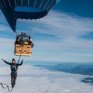 Friedi Kühne seen walking a slackline across two air balloons, the blue sky and clouds in the distance