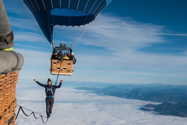 Friedi Kühne seen walking a slackline across two air balloons, the blue sky and clouds in the distance