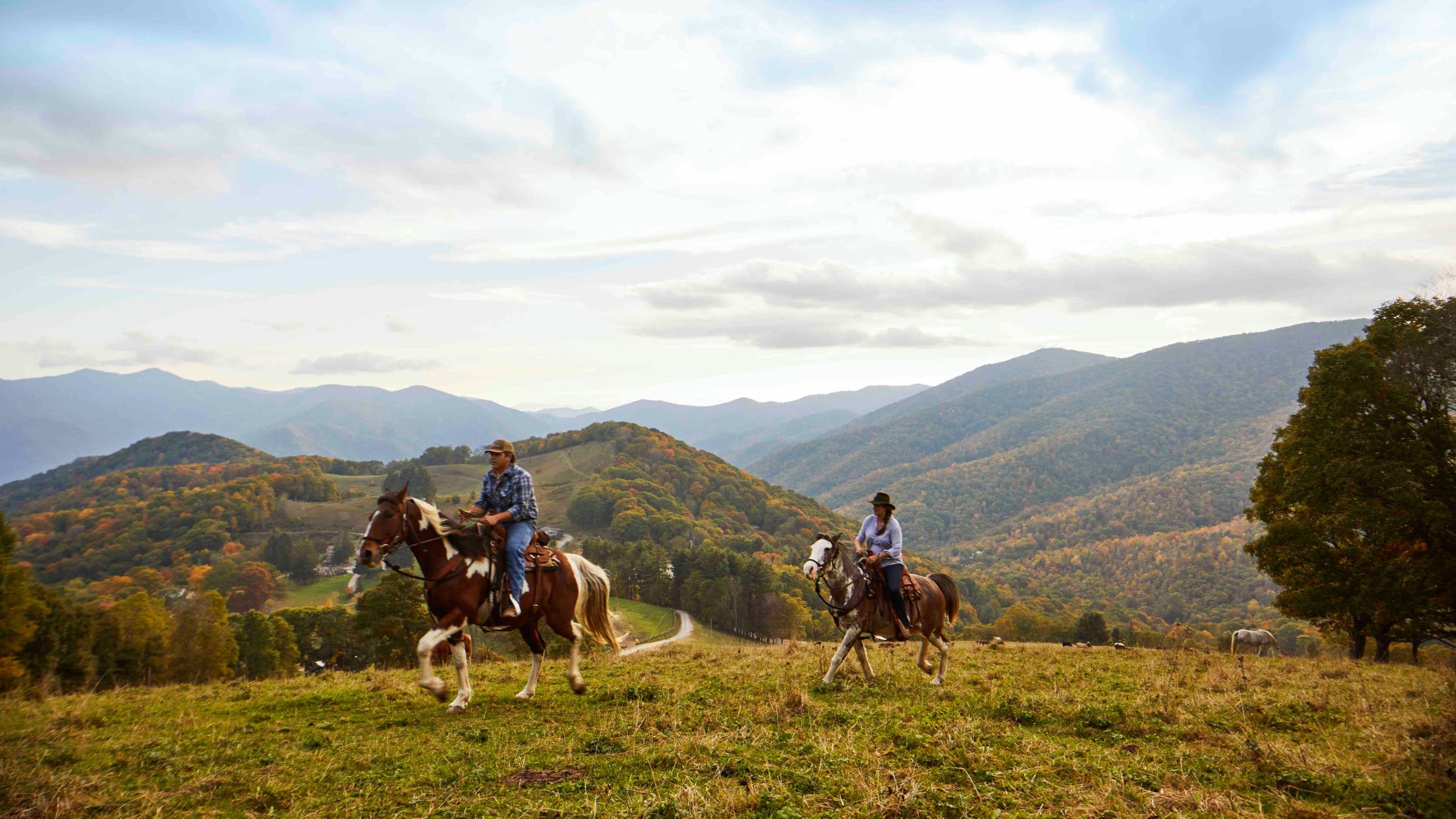 People ride across low mountains on horseback.