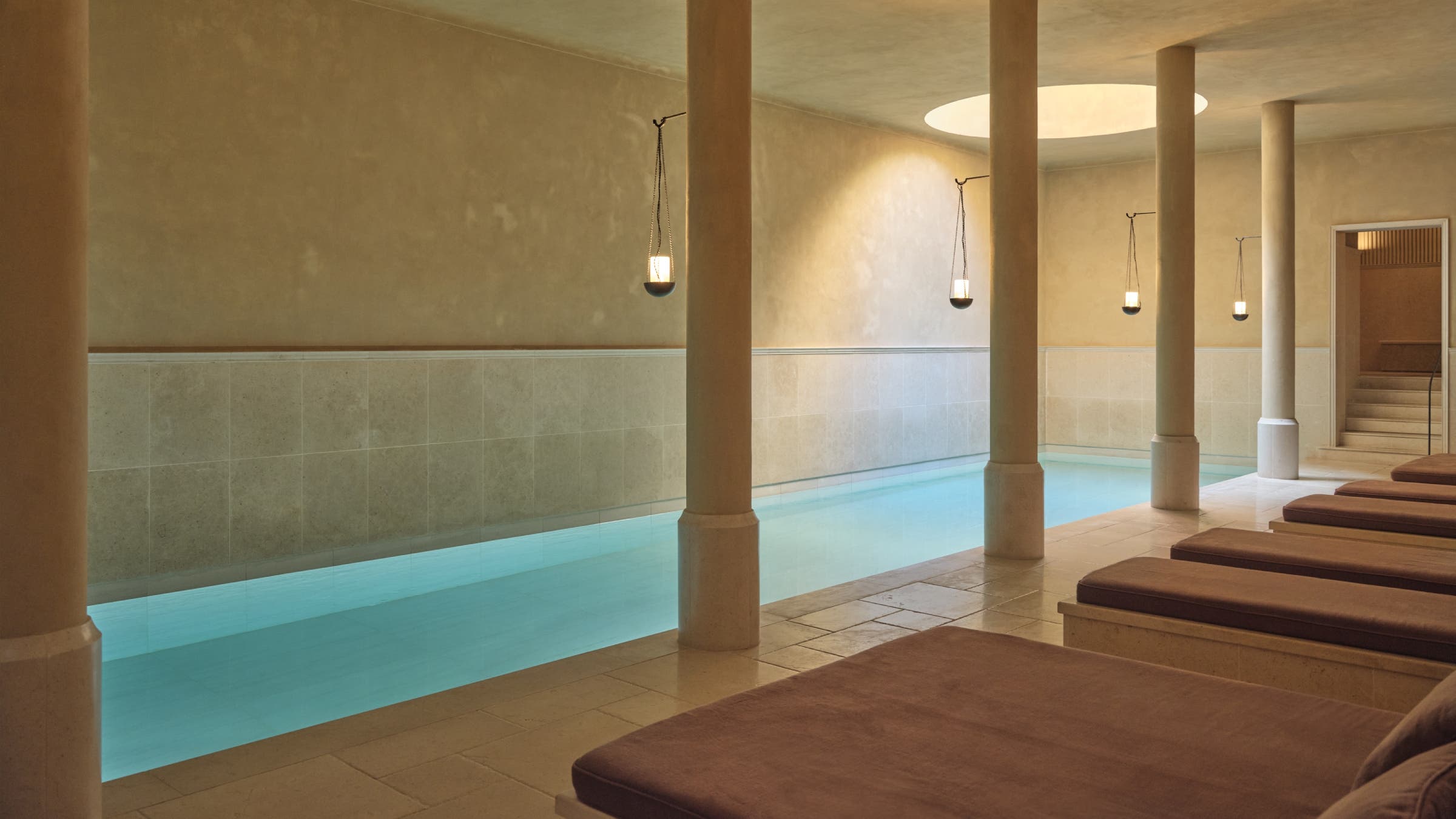 A minimalist indoor pool with sunlight shining through a circular skylight.