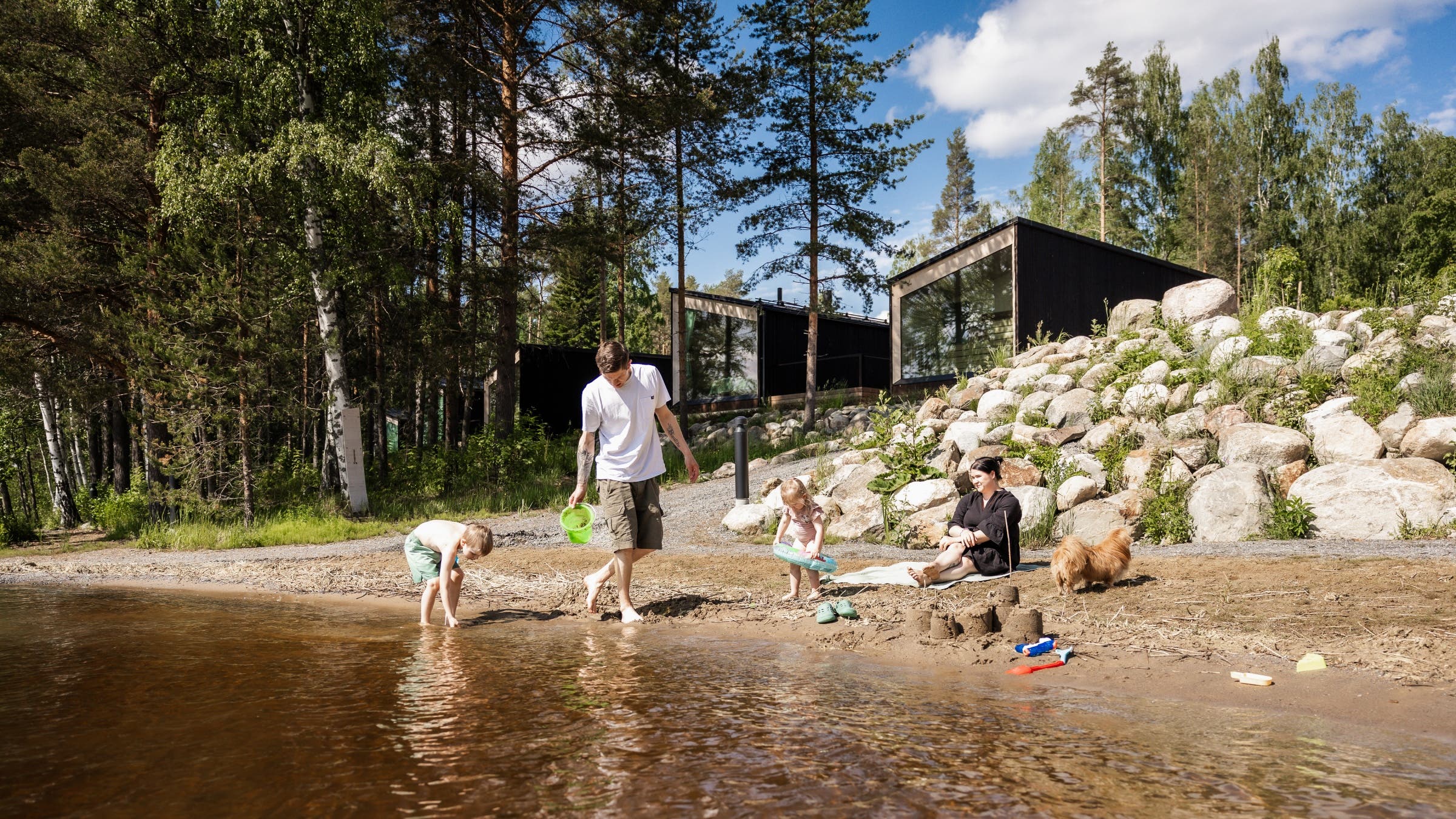 A family plays on a lakeshore outside of luxury cabins.