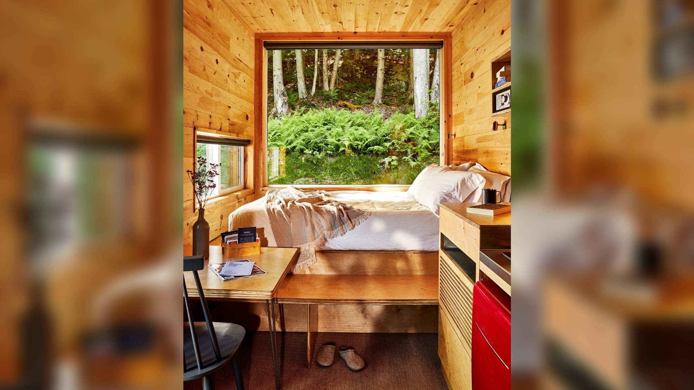 A bed in front of a large window in a small cabin.
