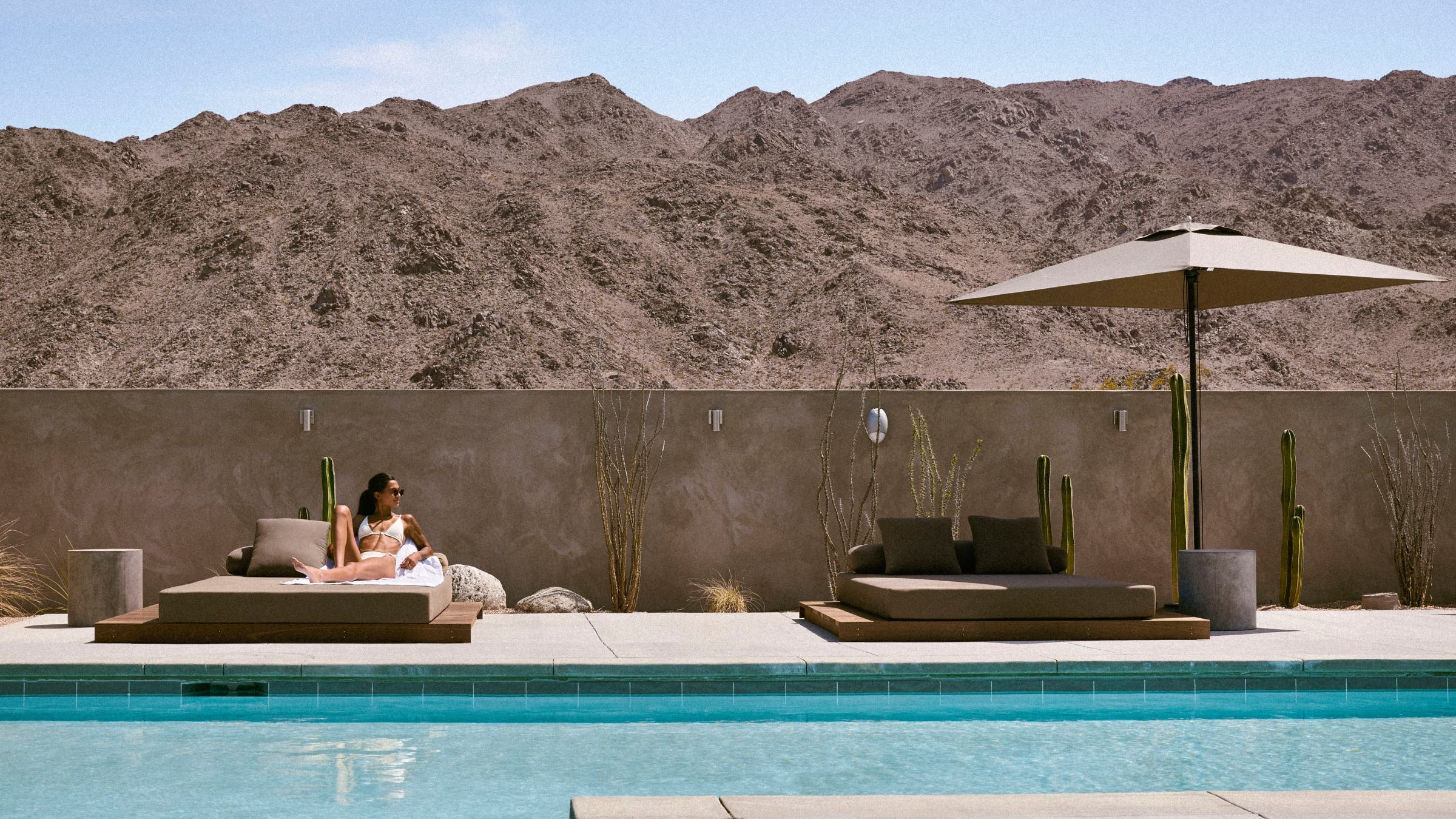 A woman lounges by a pool in a desert landscape.