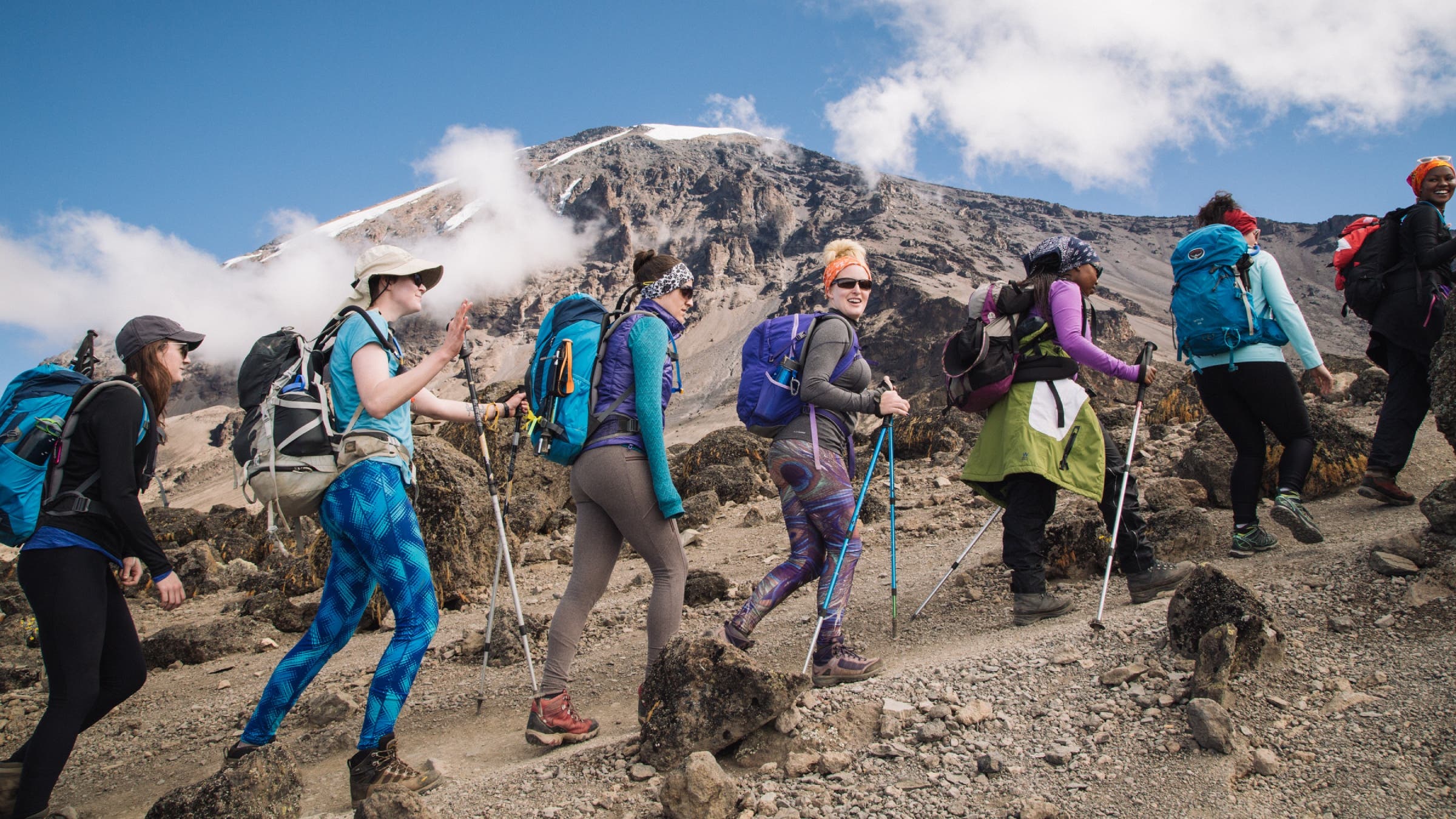 A line of women hikers trekking in front of a bare mountain peak.