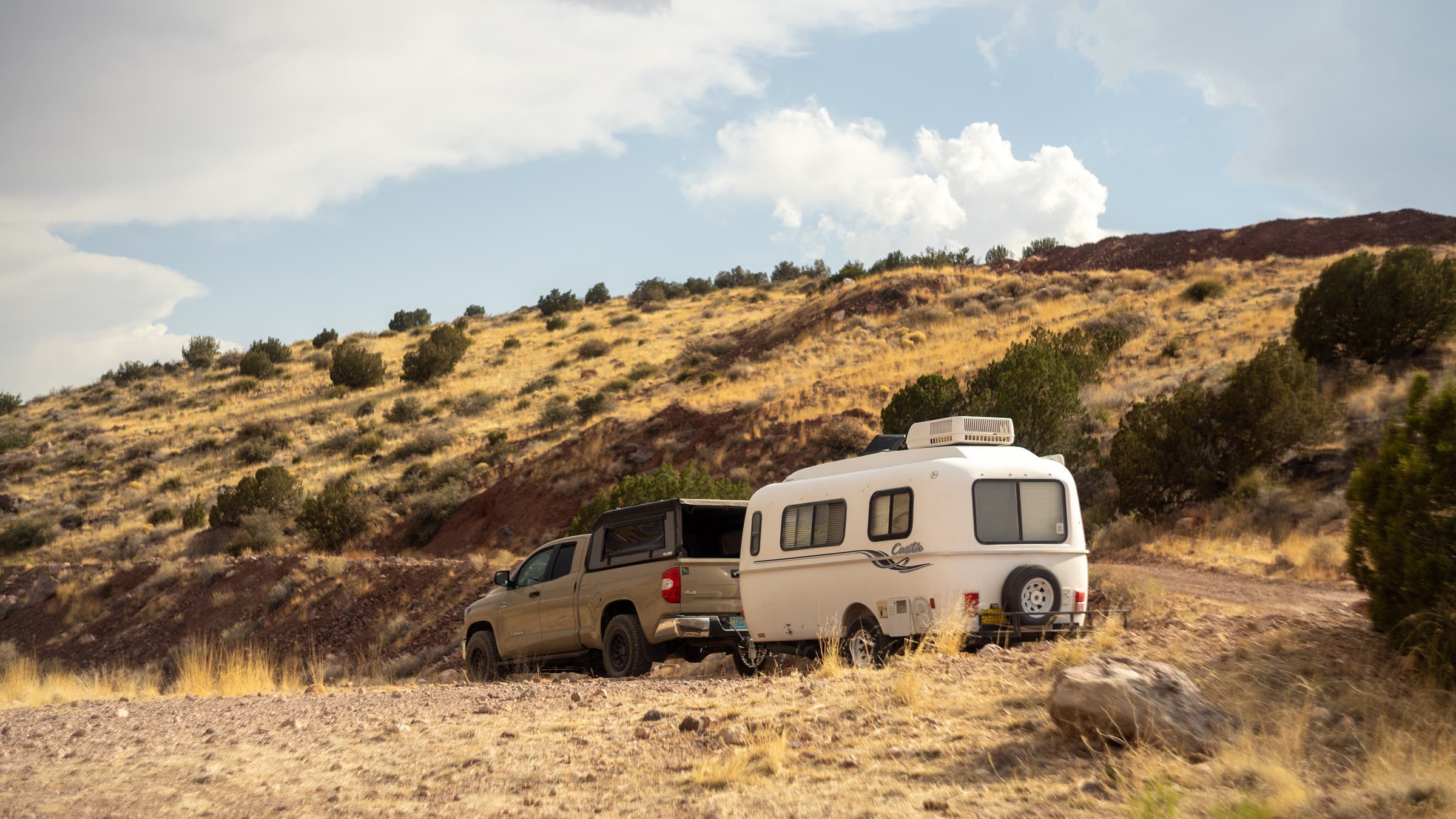 A lifted overland pickup truck carrying camper trailer behind it driving through rugged terrain.