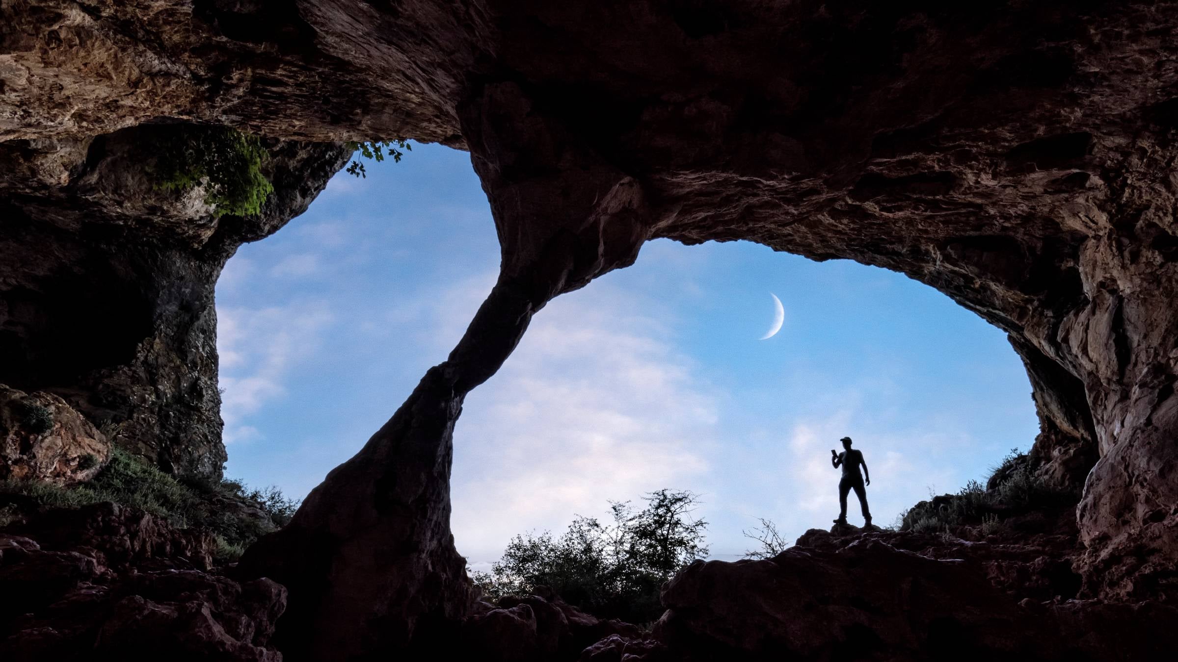 Man stands in front of dark cave