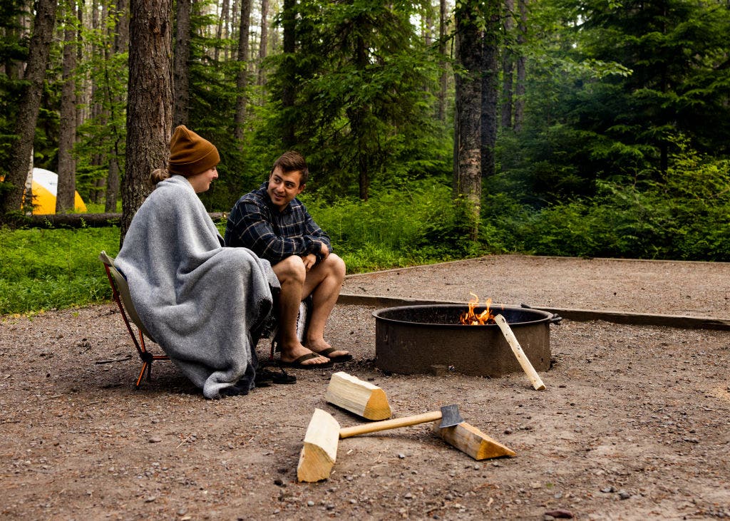 Two campers warm up around a campfire