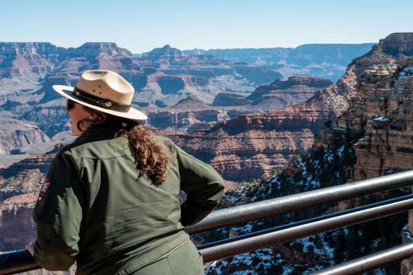a person wearing a nps uniform stares over at the grand canyon