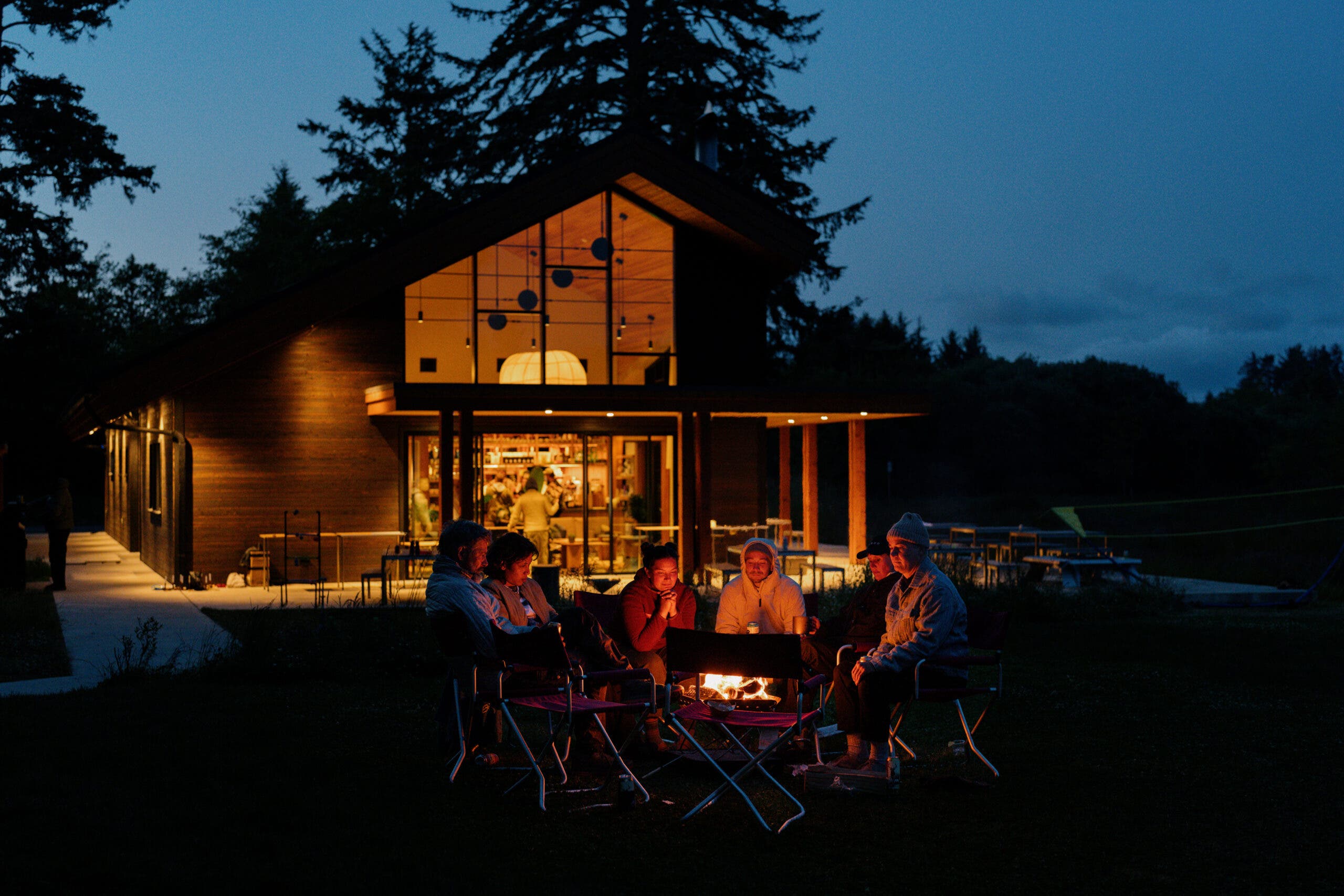 Campers sit around a fire outside at Snowpeak Campfield.