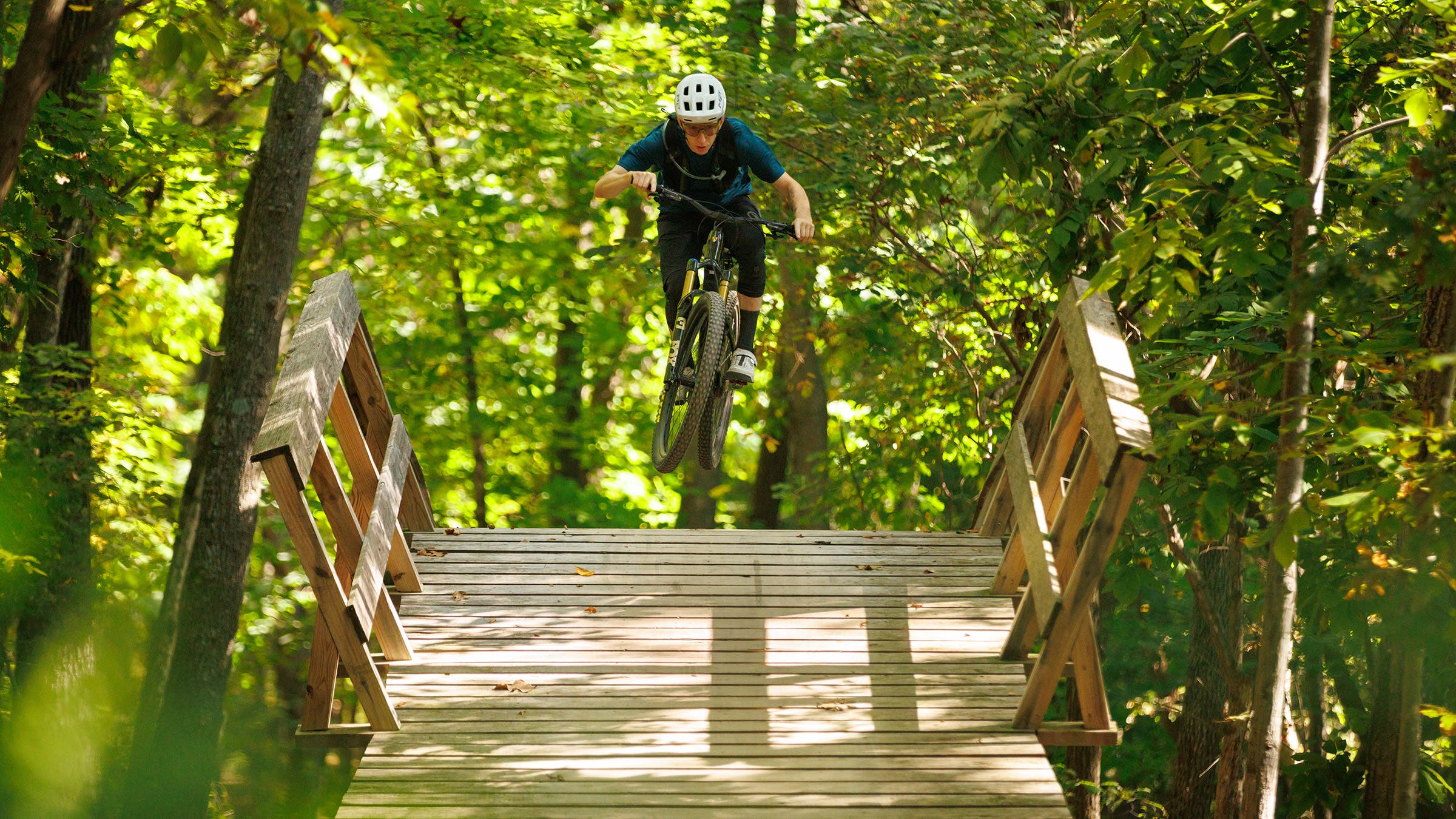 Mountain biker mid-jump on Trek Fuel EX trail mountain bike over wooden bridge
