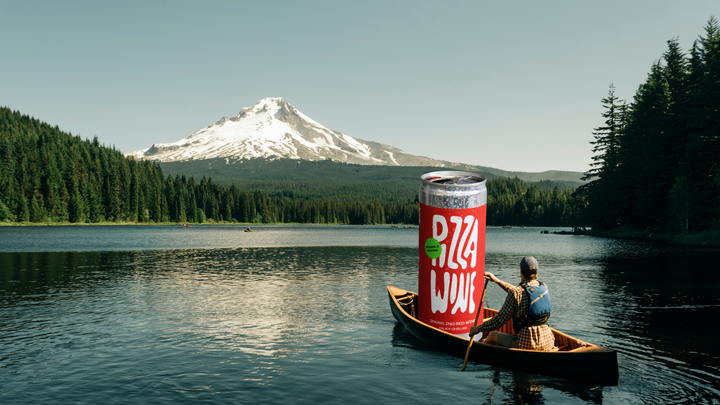 man canoes out across lake with an illustration of a large can of wine in the boat with him with mount hood in the background