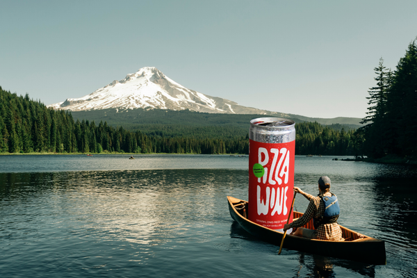 man canoes out across lake with an illustration of a large can of wine in the boat with him with mount hood in the background