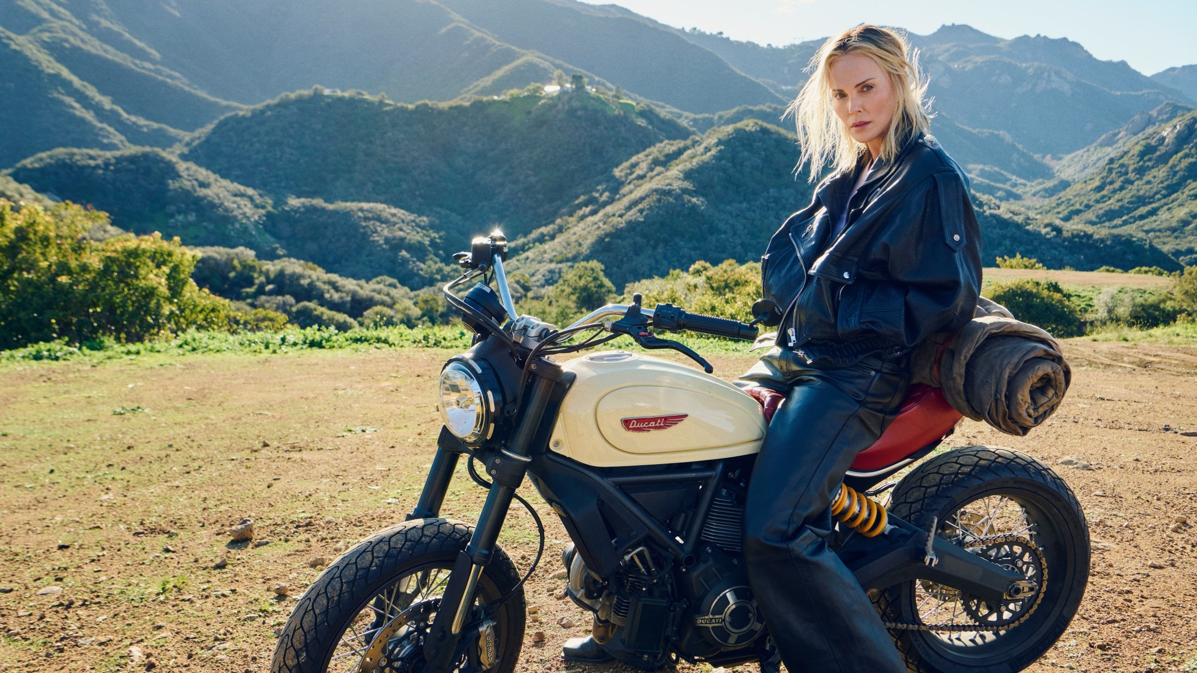 Charlize Theron sitting on a Ducati in the mountains.