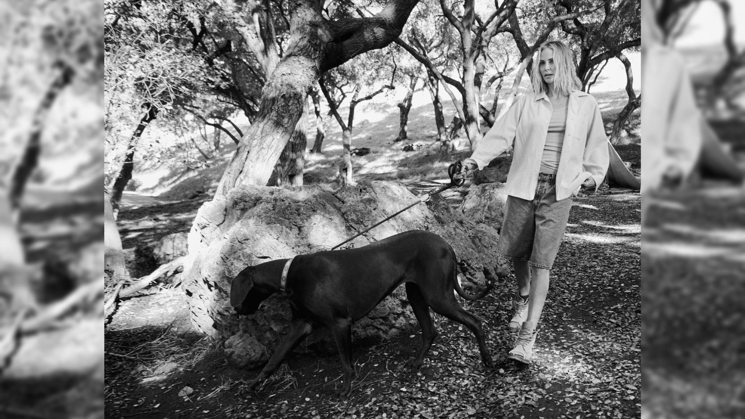 Charlize Theron walking with her dog among trees.