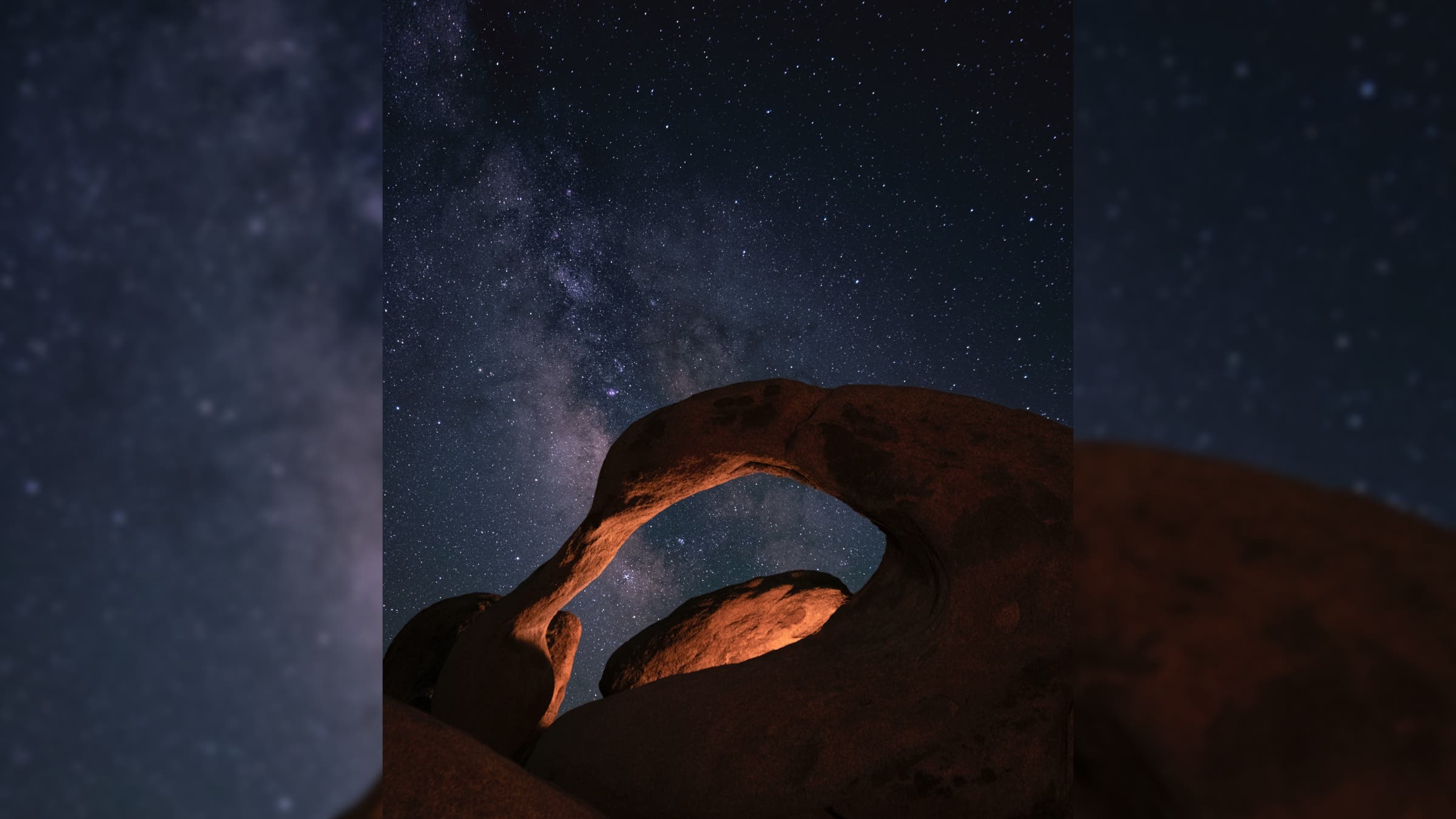 The Milky Way above a curving arch of red rock.