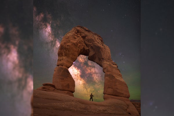 Man standing under Delicate Arch with the Milky Way behind.