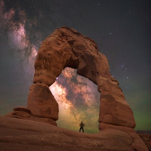 Man standing under Delicate Arch with the Milky Way behind.