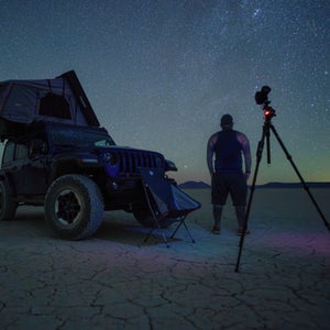 Man photographing a clear night sky on a dry lakebed.