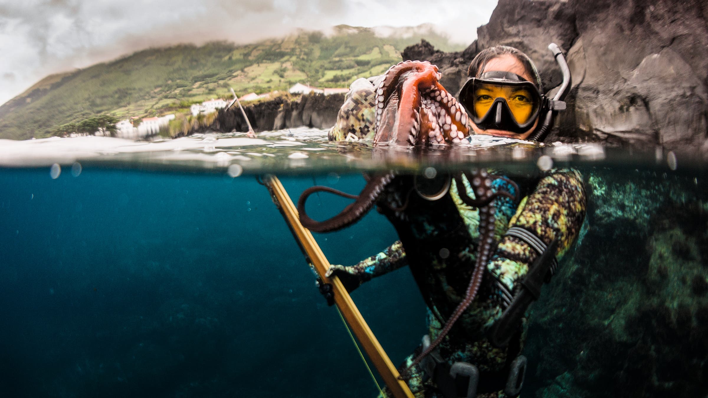 Image half-in and half-out of the water showing Kimi Werner holding up an octopus.