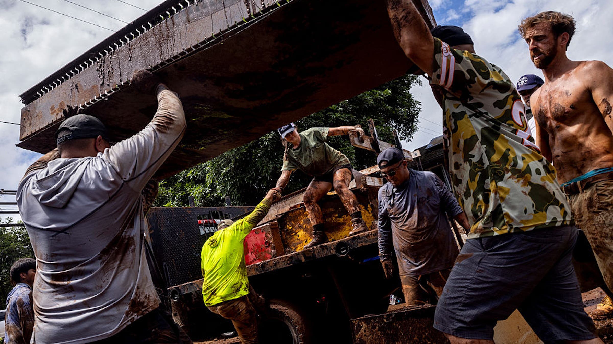 Kali Retzler, center, pulls Geoffrey Browne onto a truck as fellow volunteers carry debris from a home impacted by the flood in Haleiwa, Hawaii