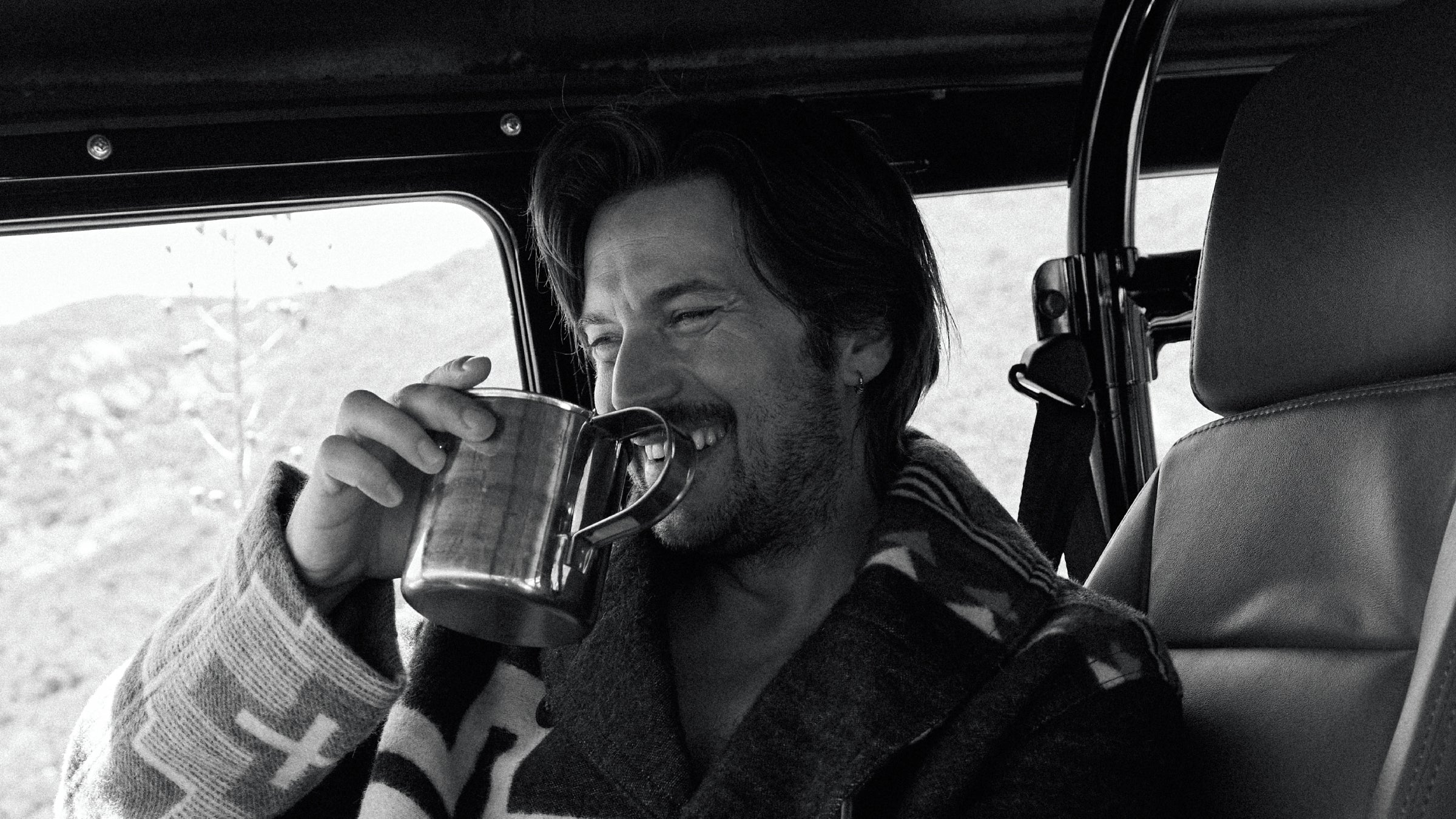 Lucas Bravo smiles while sitting in a car.