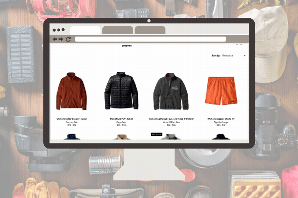 A desktop computer screen displays the Patagonia Worn Wear website, featuring a grid of various used outdoor gear such as puffer jackets, fleece pullovers, and hiking shorts. The monitor is set against a background of organized camping equipment, including ropes, a headlamp, and a water bottle.