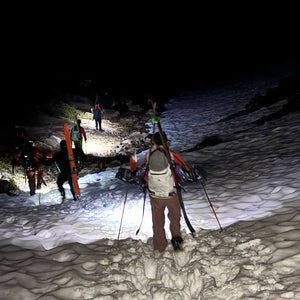 a team of search and rescue personnel hike through the snow with skis packed on their back