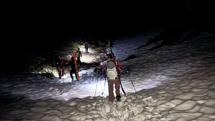 a team of search and rescue personnel hike through the snow with skis packed on their back