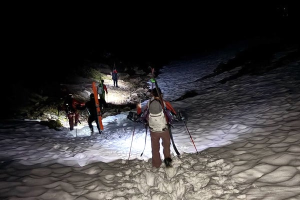 a team of search and rescue personnel hike through the snow with skis packed on their back