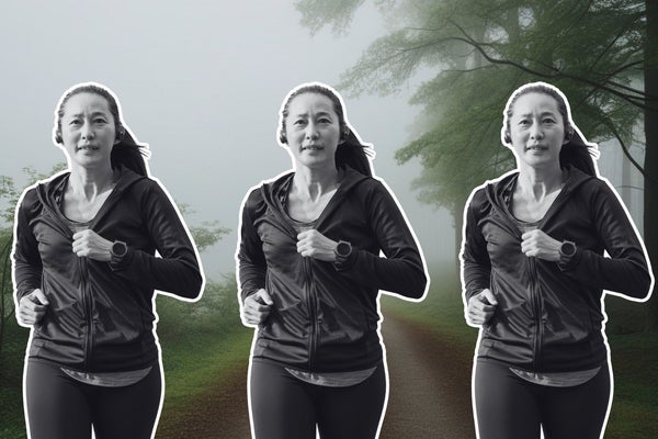 An older Asian woman running on a forest running trail behind her.