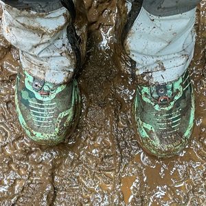 person wearing muddy hiking boots, standing on a muddy trail