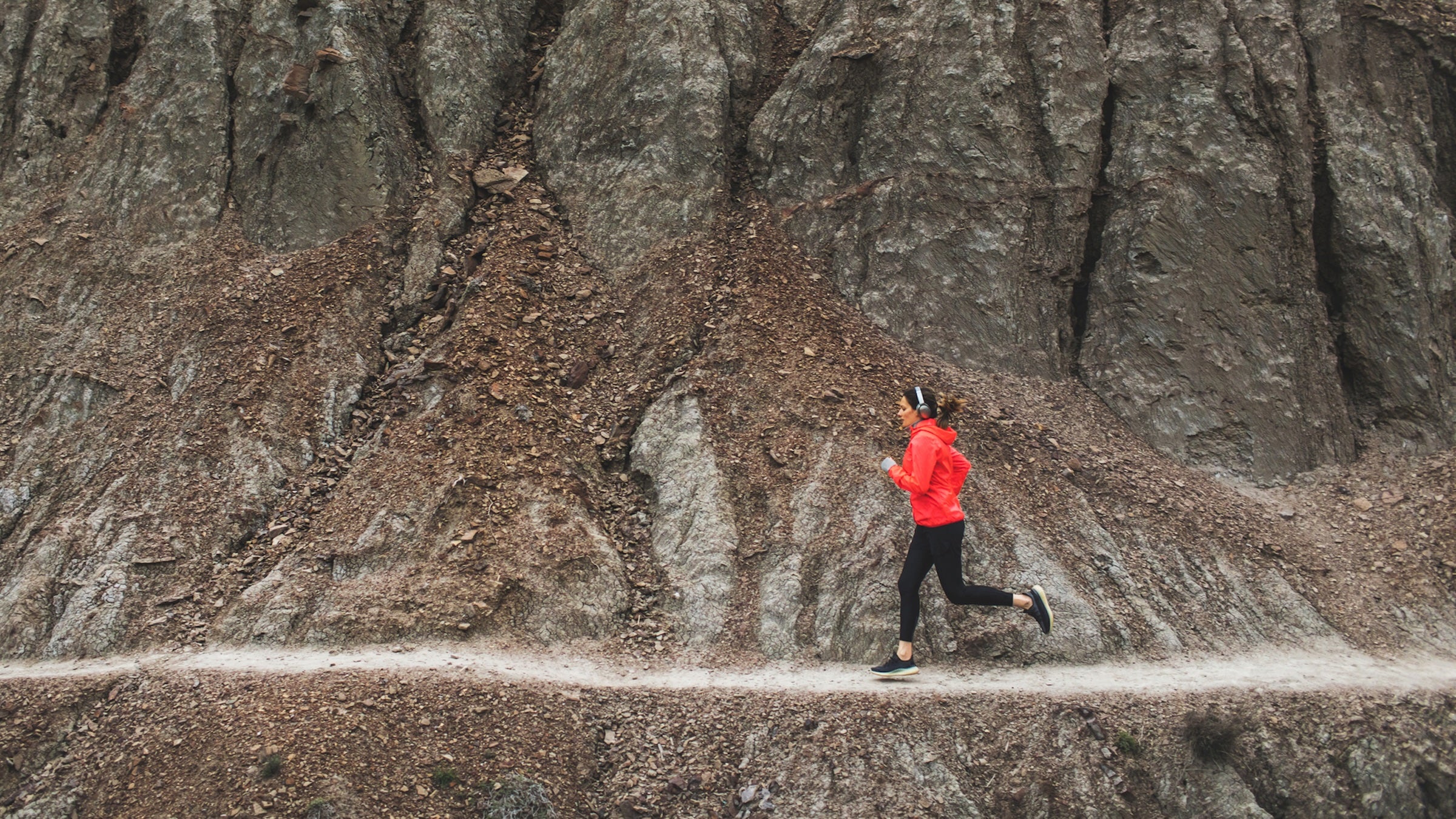 woman running on rocky singltrack in red jacket