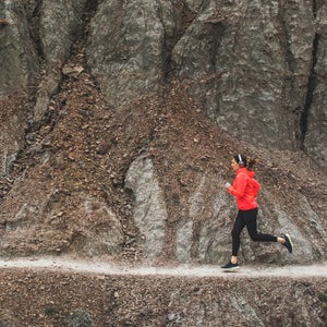 woman running on rocky singltrack in red jacket