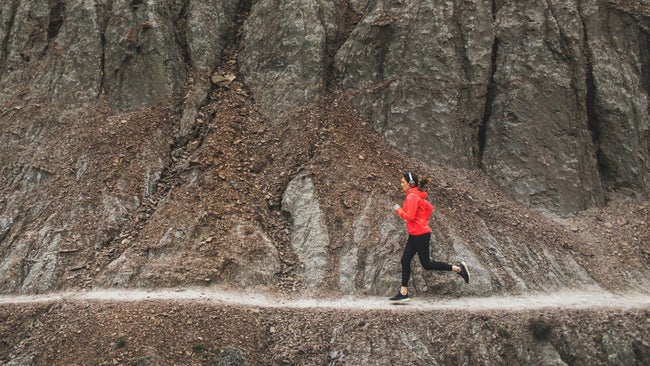 woman running on rocky singltrack in red jacket