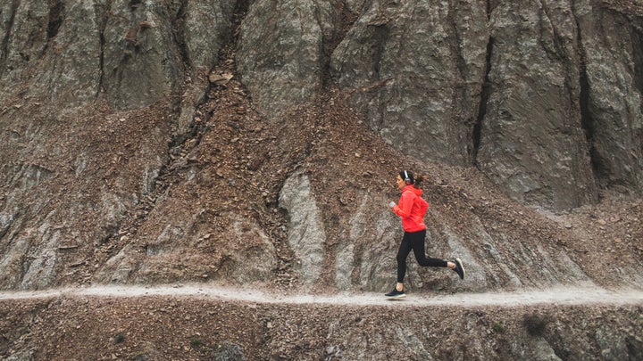 woman running on rocky singltrack in red jacket
