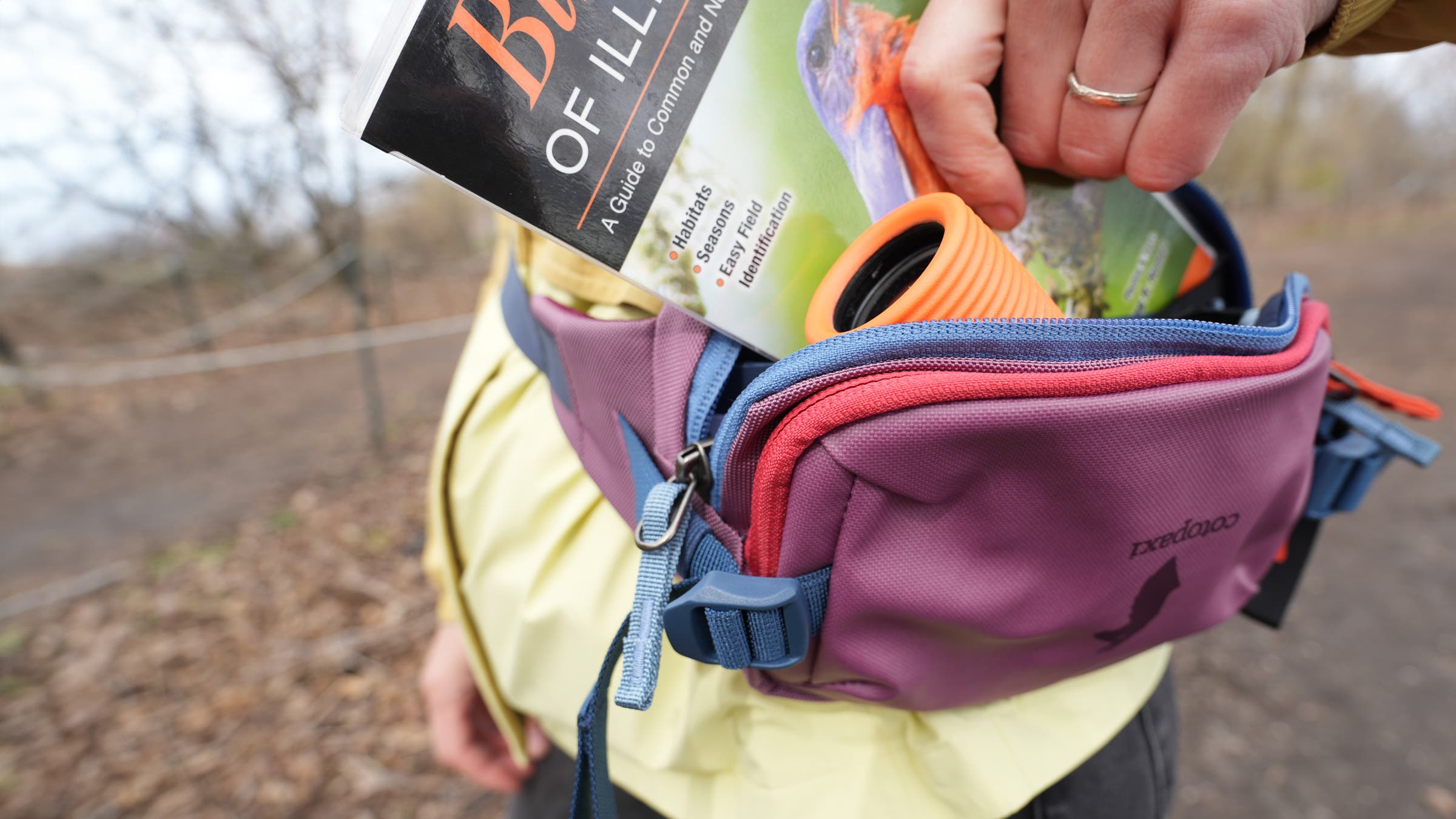 Hiker with Nocs monocular and birding guidebook in Cotopaxi Hip Pack, an essential piece of the best birding gear
