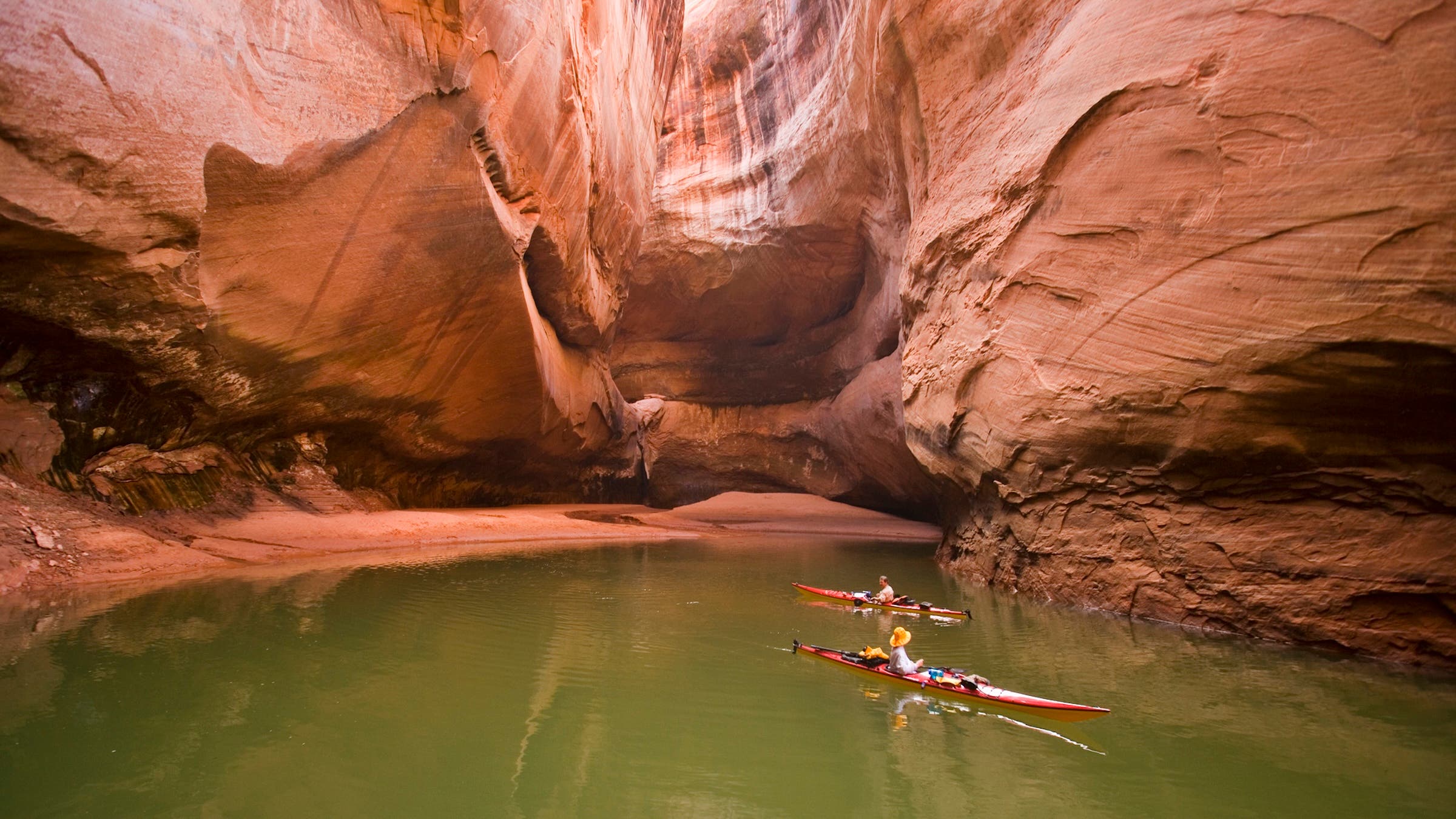 two kayakers are seen paddling through lake powell's red canyon walls, juxtaposed next to green lake water