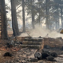 A firefighter stands near smoldering debris and active flames amid the charred remains of burned structures near the Grand Canyon Lodge at Grand Canyon National Park on July 13, 2025