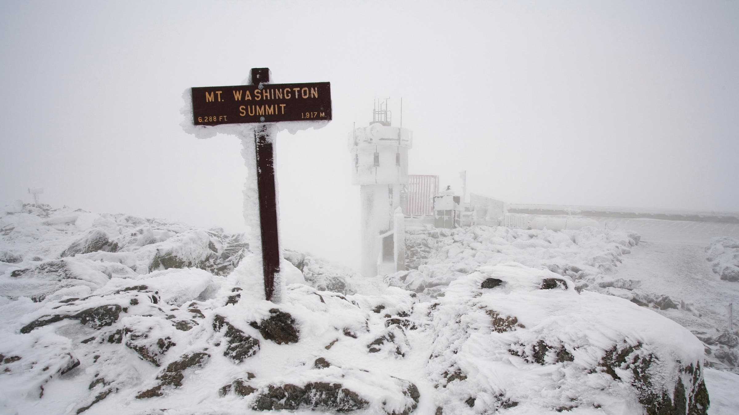 A snow and ice covered sign marks the summit of Mount Washington in the White Mountains of New Hampshire
