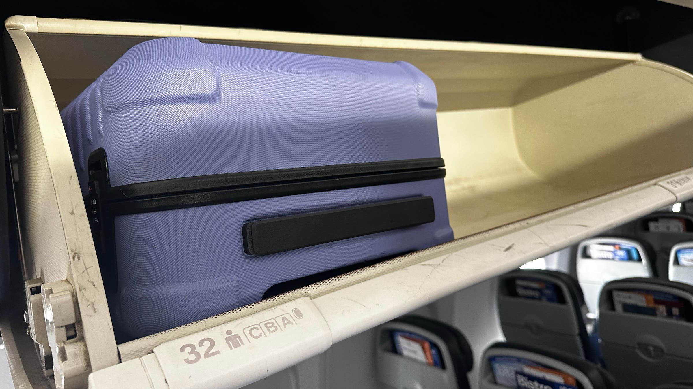 Cotopaxi hard-sided carry on suitcase fits into overhead bin on airplane.