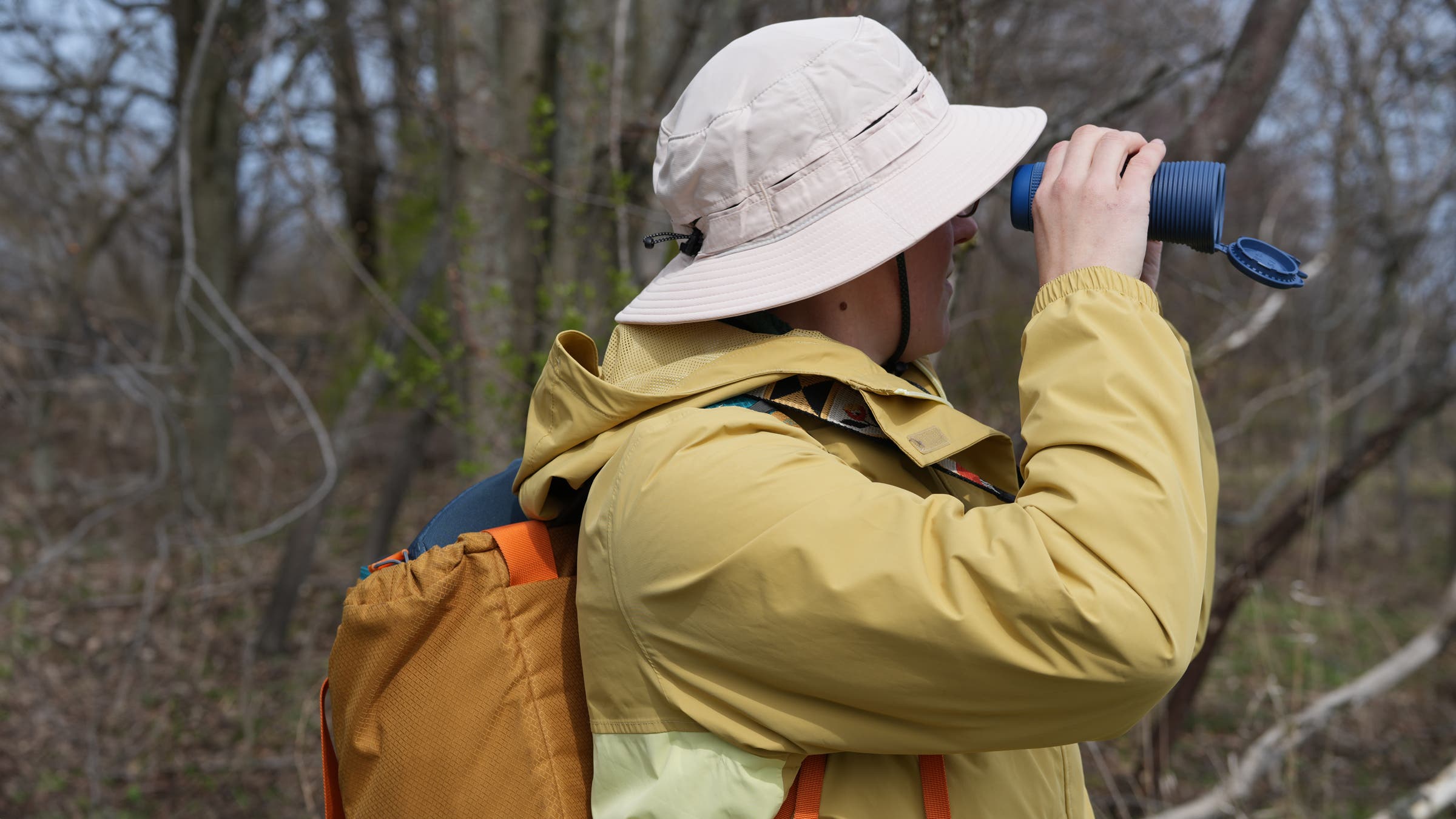 Bird watcher wearing REI Sahara Bucket Hat while birding in woods, an essential piece of the best birding gear