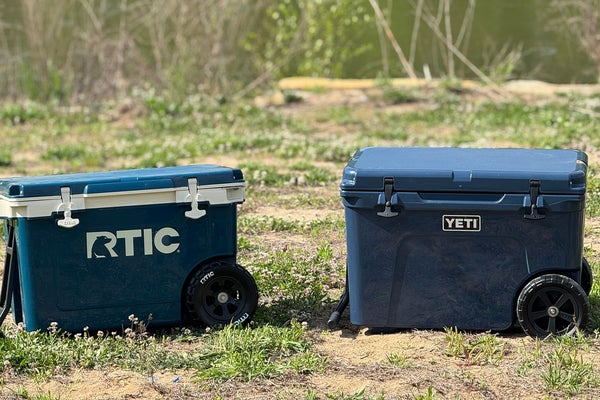 Blue RTIC Ultralight Wheeled 52 QT cooler displayed next to blue Yeti Tundra Haul wheeled cooler on grass
