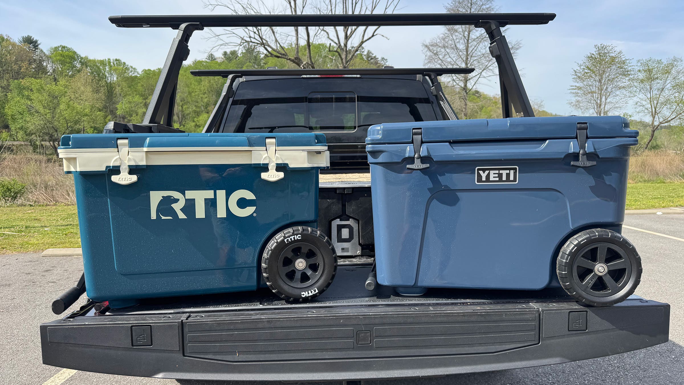 Blue RTIC Ultralight Wheeled 52 QT cooler next to blue Yeti Haul Trundra wheeled cooler on truck bed